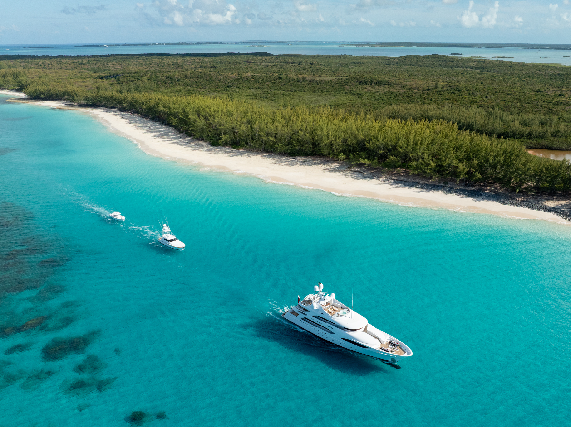 Aerial wide of Motor Yacht Avalon anchored beside a Bahamian beach with sportfish tenders