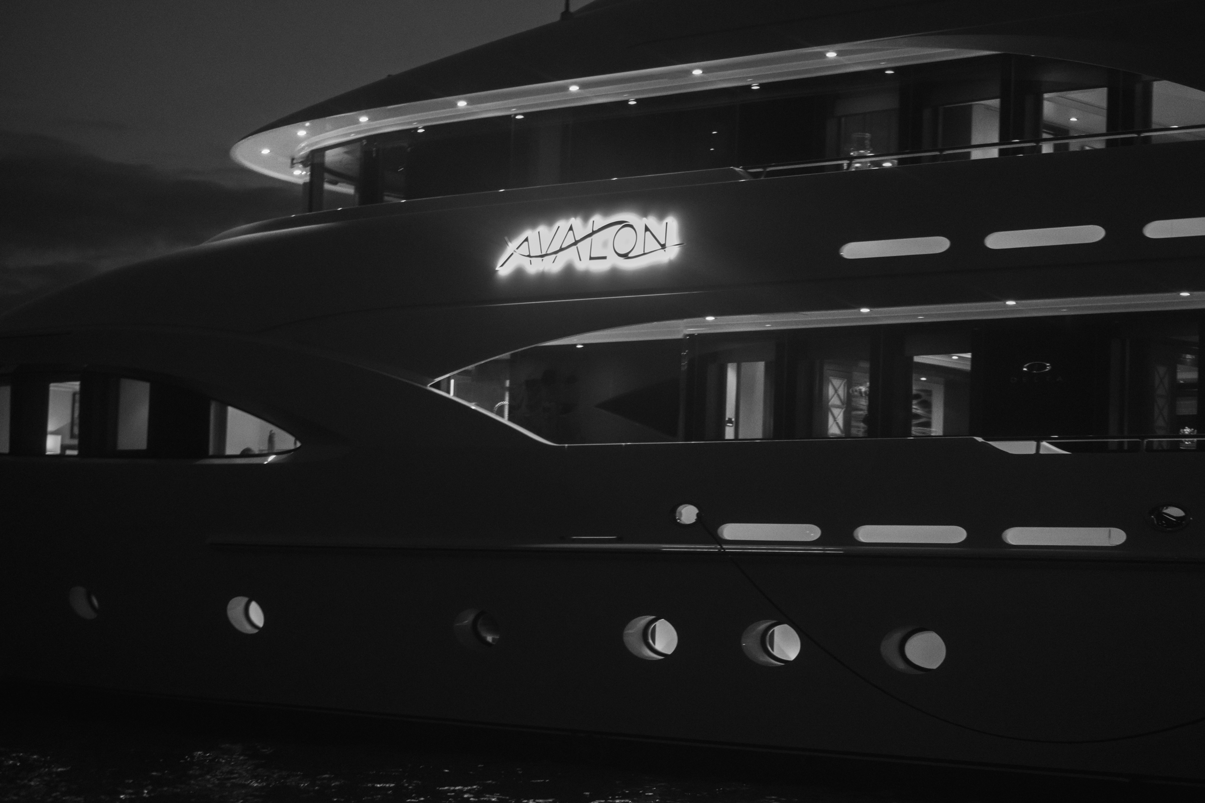 Motor Yacht Avalon's full profile illuminated against the night — name signage lit, deck lights warm
