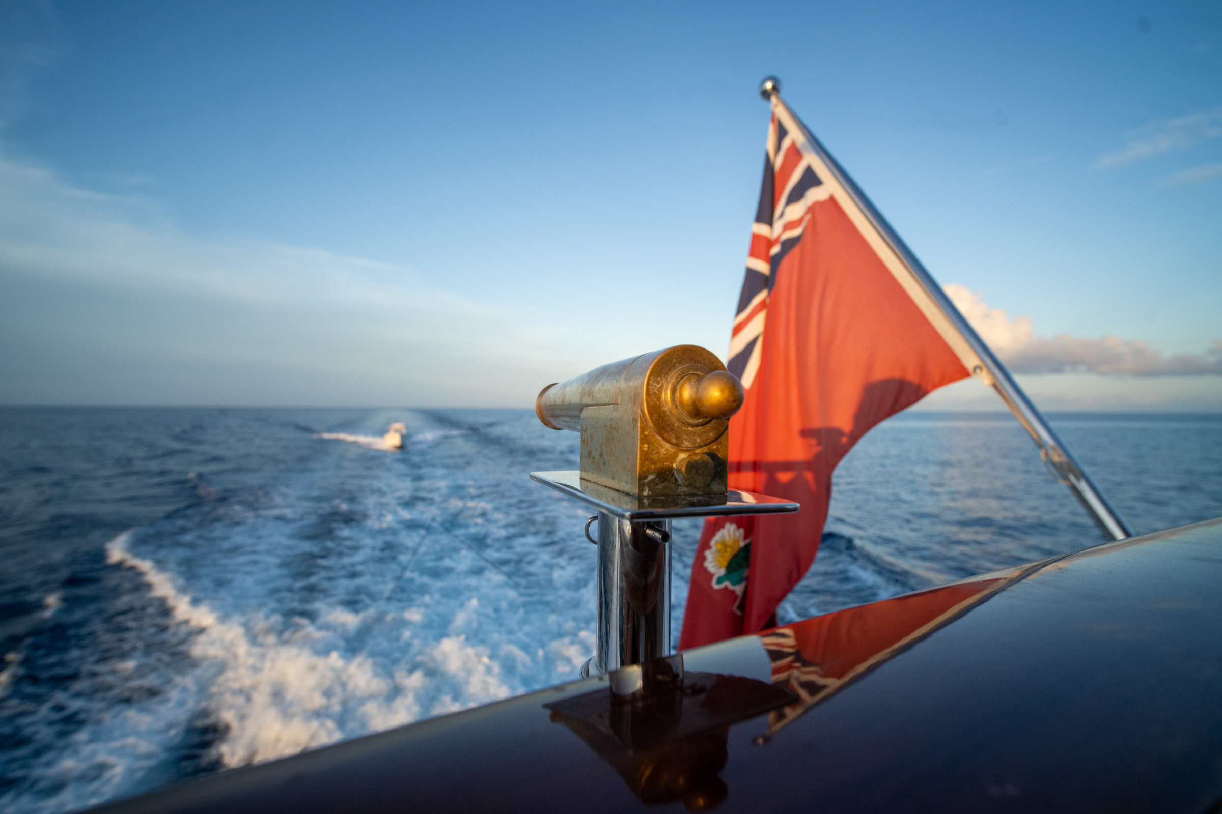 Red ensign and brass detail above Motor Yacht Avalon's wake at golden hour