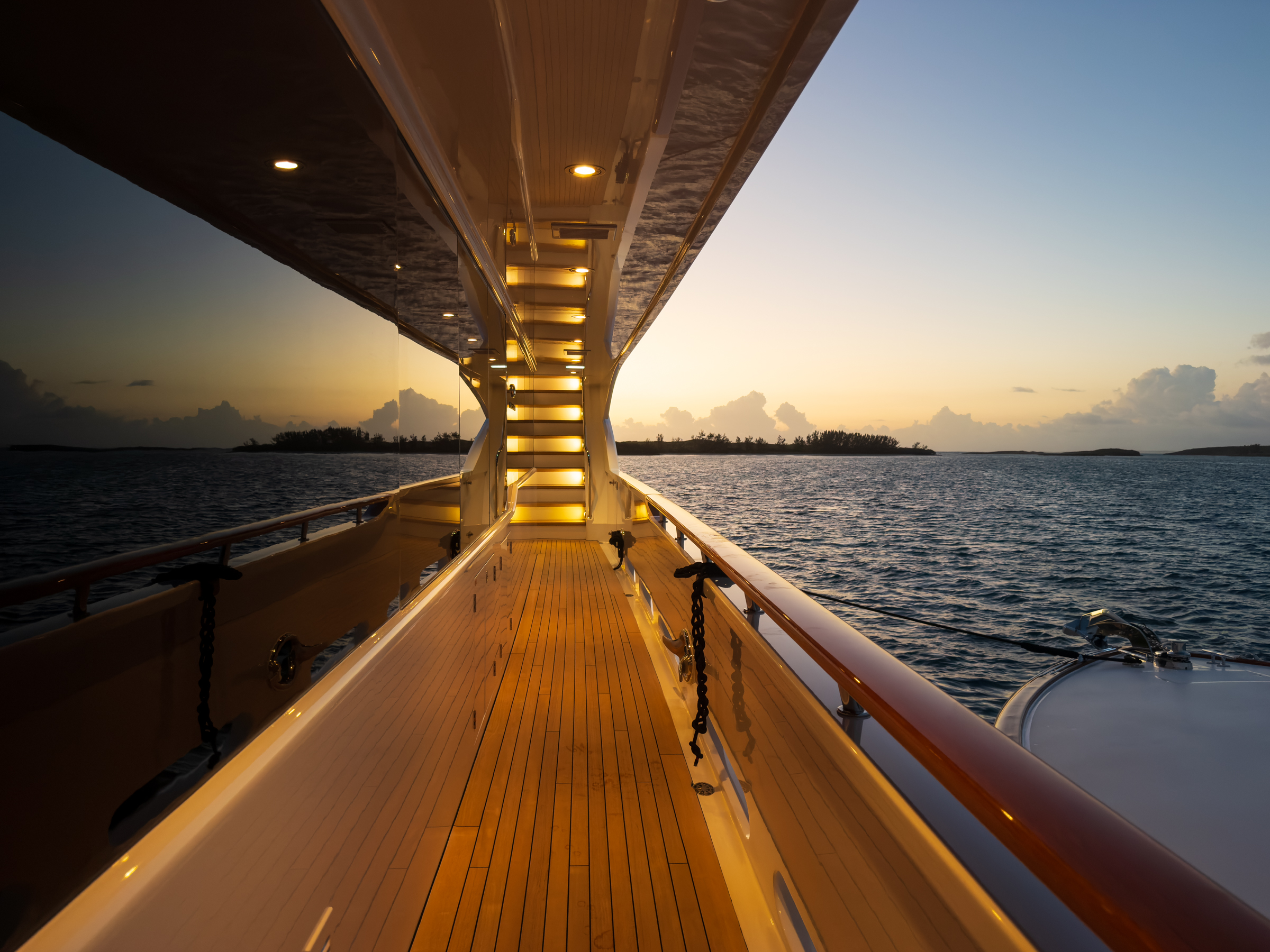 Warmly lit teak side deck leading toward a Bahamian sunset aboard Motor Yacht Avalon